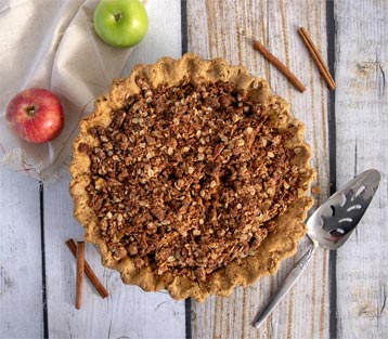 Apple pecan pie on table with two apples and serving spoon